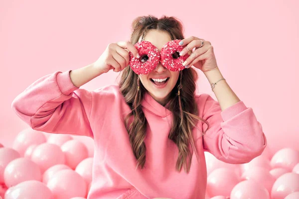 Sorrindo bela mulher se divertindo com donuts sobre fundo rosa — Fotografia de Stock