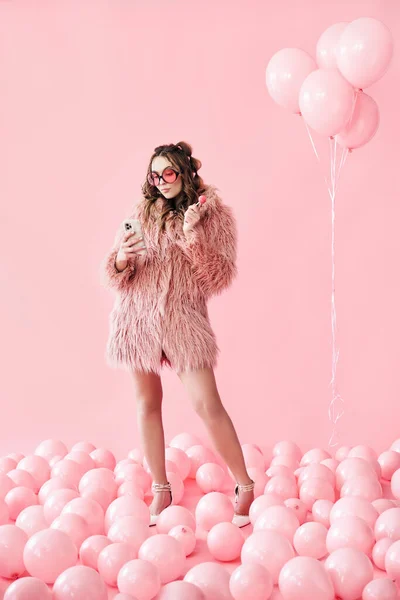 Retrato de comprimento total de glamour jovem digitando no smartphone móvel sobre fundo balões rosa — Fotografia de Stock
