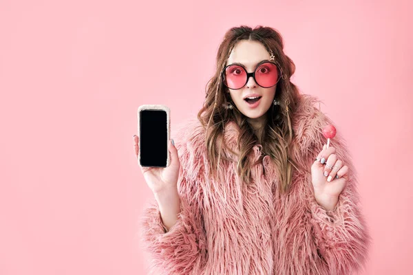 Mujer hipster sorprendida sosteniendo pantalla en blanco teléfono móvil sobre fondo rosa — Foto de Stock