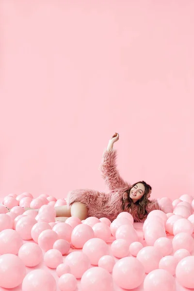 Retrato de moda de mujer bonita sonriente acostada en muchos globos rosados sobre fondo pastel rosado —  Fotos de Stock