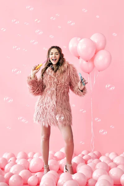 Junge hübsche Frau hat Spaß mit Seifenblasen auf rosa Hintergrund mit Luftballons — Stockfoto