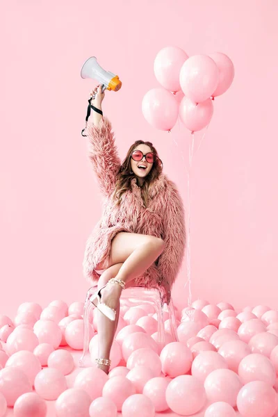 Mujer sonriente de moda sosteniendo megáfono sobre fondo de globos rosados —  Fotos de Stock