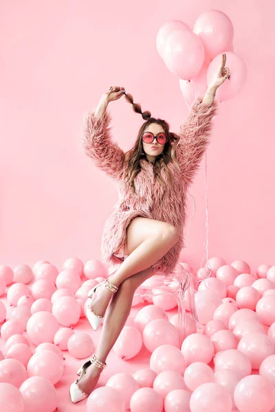 Mujer de moda feliz posando sentado en la silla en muchos globos de color rosa de fondo —  Fotos de Stock