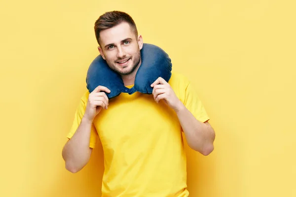 Junger Mann mit Reisekissen auf gelbem Hintergrund — Stockfoto