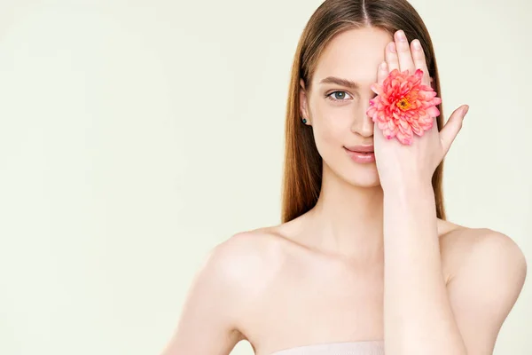 Close up portrait of beautiful young woman covering her eye with flower — Stock Photo, Image