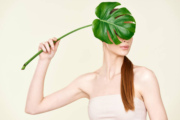 Young woman covering and hiding face with monstera tropical leaf.