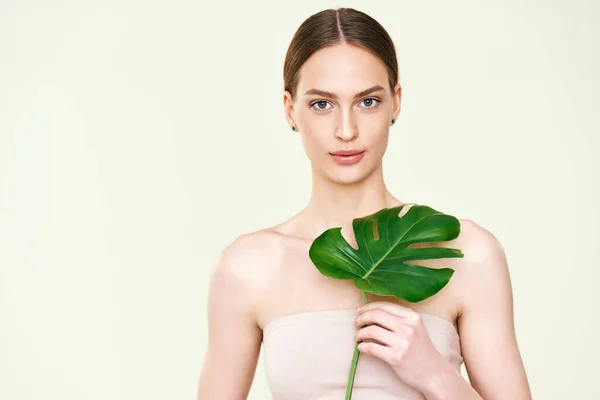 Young beautiful woman holding monstera tropical leaf with copy space — Stok fotoğraf