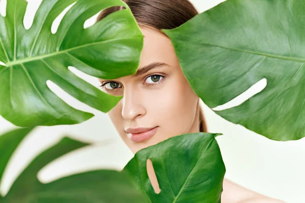 Close up portrait of young beautiful woman with perfect smooth skin in tropical leaves — Stok fotoğraf