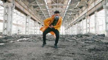 Koruyucu maskeli genç erkek dansçı harap olmuş binada serbest stil dansı yapıyor.