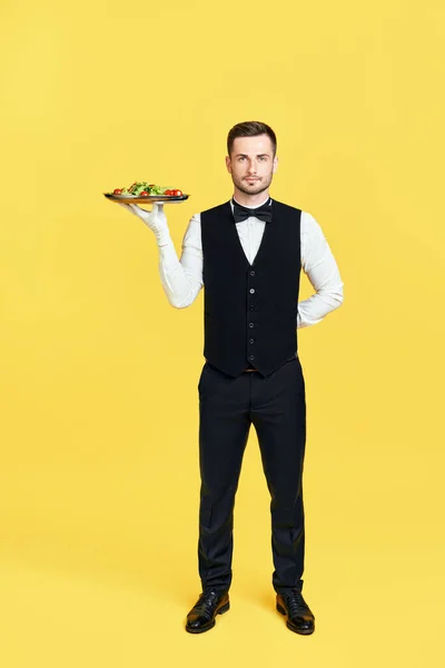 ull length portrait of smiling waiter holding plate with healthy vegetable salad ready to serve