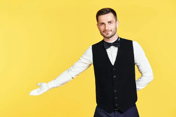 Young handsome waiter doing a welcome gesture over yellow background — Stock Photo, Image