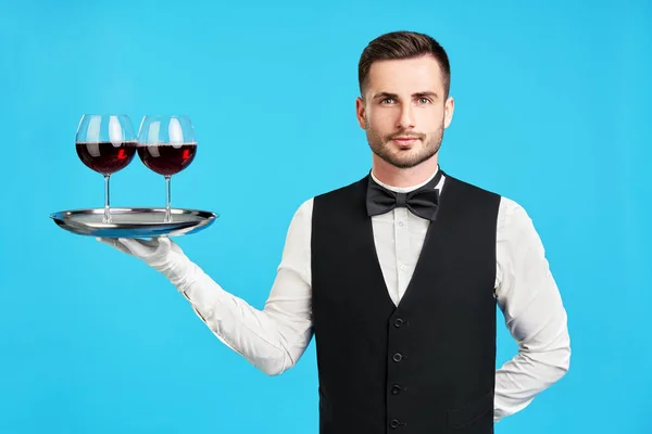 Garçom masculino elegante com copos de vinho sobre fundo azul — Fotografia de Stock