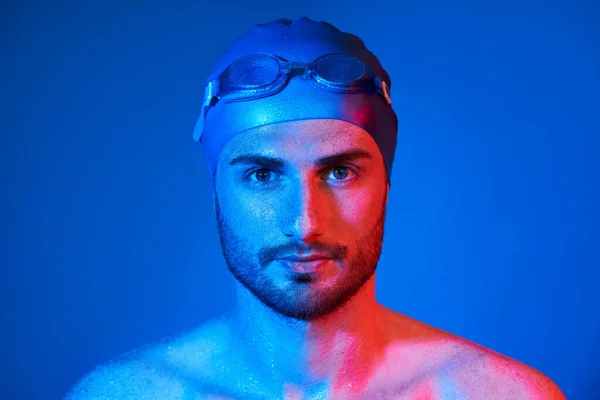 Retrato de cerca del apuesto nadador con gafas en luz de neón rojo-rosa sobre fondo azul —  Fotos de Stock
