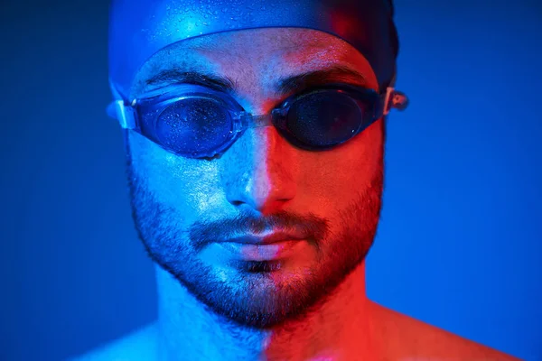 Retrato de cerca del apuesto nadador con gafas en luz de neón rojo-rosa sobre fondo azul —  Fotos de Stock