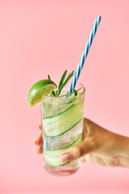 Genç bir kadın pembe arka planda bardakta soğuk kokteyl tutuyor.