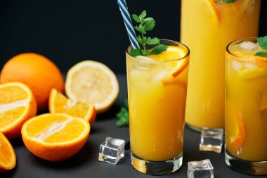 Lezzetli taze portakal suyu, buz, nane ve siyah masa arkasında taze meyveler.