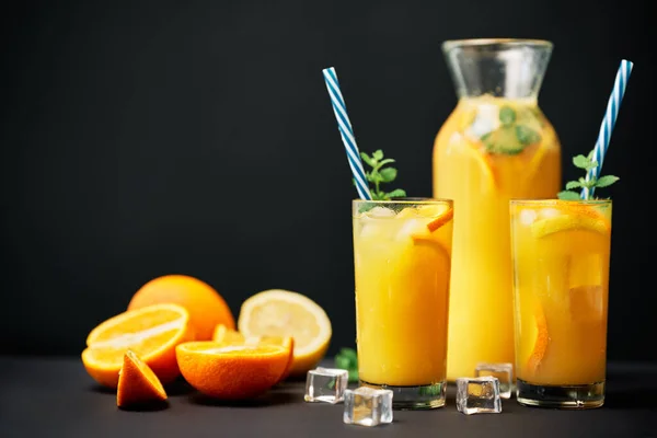 Delicious orange juice with ice, mint and fresh fruits on black table background with copy space