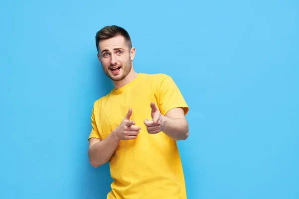 Lustiger fröhlicher Mann zeigt auf dich und blickt in die Kamera auf blauem Hintergrund — Stockfoto