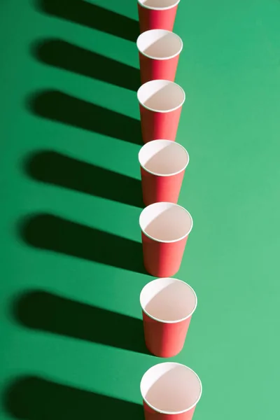Вид сверху красной бумажной чашки подряд на зеленом фоне с тенями — стоковое фото