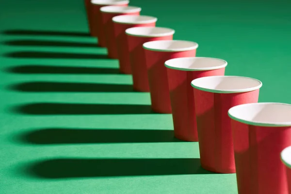 Prospettiva decrescente di tazza di carta rossa in fila su sfondo verde con ombre — Foto Stock
