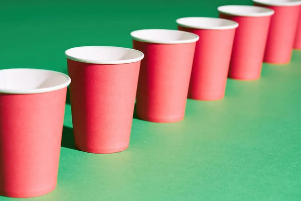 Perspectiva atenuante de la taza de papel rojo en fila sobre fondo verde — Foto de Stock