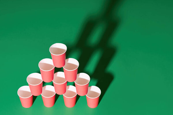 Pyramid of red paper cups on green background with copy space