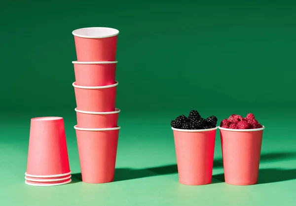 Frische Beeren in roter Tasse auf grünem Hintergrund und Einweg-Pappbecher — Stockfoto