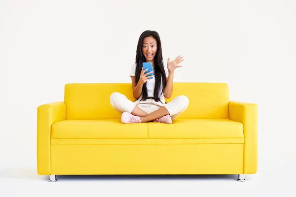 Émotionnel surpris asiatique femme réception bon message sur cellulaire assis sur jaune canapé — Photo