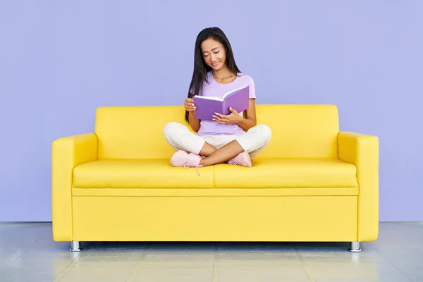 Прелестная женщина, читающая книгу, сидя на уютном желтом диване, понятия о доме и комфорте — стоковое фото