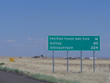 Arizona yolundaki yön tabelasında Petrified Forest Ulusal Parkı, Gallup ve Albuquerque 'ye uzaklık bilgisi var..