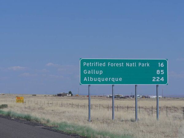 Directional sign on the road in Arizona with distance information to the Petrified Forest National Park, Gallup and Albuquerque.