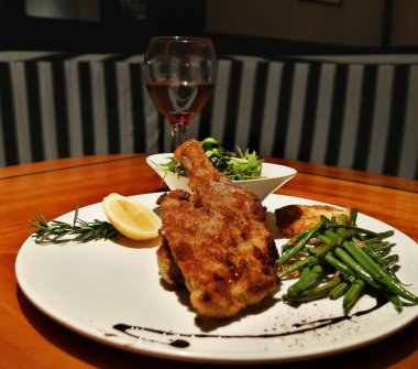 Kızarmış tavuk, yeşil fasulye ve sebze salatası, kırmızı şarapla servis edilir. 