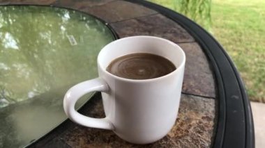 Dairesel cam tepeli bir masada el kamerasıyla çekilmiş bir fincan kahve.