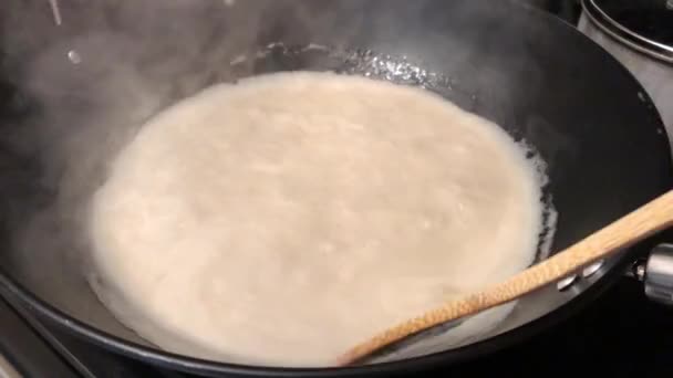 Hand-held shot van een hand roeren kokosmelk koken in een grote pan — Stockvideo