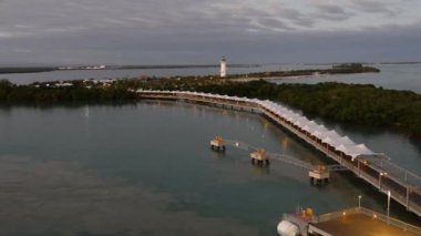 Harvest Caye Adası 'ndaki deniz fenerinin el kamerası görüntüsü, alacakaranlıkta Belize, rıhtım ışıkları suya yansıyor.