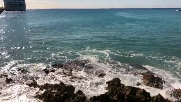 Golven rollen naar een rotsachtige kustlijn met een cruiseschip in de verte. — Stockvideo