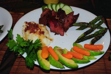 Renkli bir tabak ızgara sebze, patates salatası ve ince dilimlenmiş biftek.