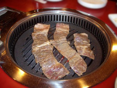 Kore restoranındaki kapalı masa ızgarasında pişen ince et dilimleri..