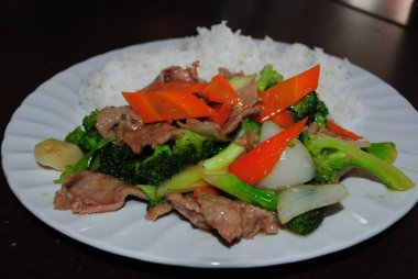 Sotelenmiş biftek ve brokoli, yanında da beyaz tabakta pirinç..