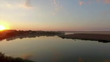 Yeşil alanlarda büyük bir nehir üzerinde renkli günbatımı güzel havadan görünümü 