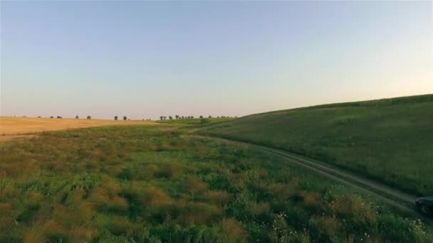 Вид с воздуха на автомобиль, движущийся по проселочной дороге между полями с большой рекой на заднем плане — стоковое видео