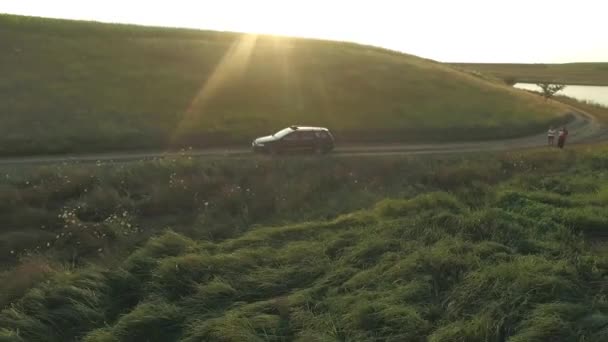 Vista aérea de um carro dirigindo em uma estrada rural entre campos com um grande rio no fundo — Vídeo de Stock