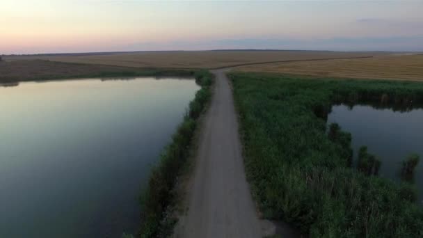 एक निर्जन देश सड़क सूर्यास्त पर दो झीलों से गुजर रही है — स्टॉक वीडियो