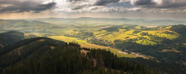 Ormanlı tepelerle çevrili yeşil bir vadi manzarası.