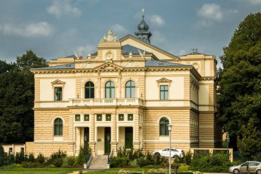 Şehir merkezinde bir caddede duran ağaçlarla çevrili eski bina.