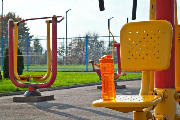 Oranje Fles Met Water Achtergrond Van Sportuitrusting Gele Rode Straatsimulatoren — Stockfoto