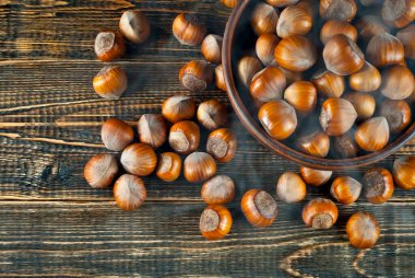 Kahverengi ahşap arka planda bir kasede fındık. Eski püskü bir tahtada bir sürü fındık var. Masada mavi duman ve buhar.