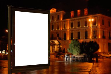Gece şehrinin arka planında boş tabela var. Tasarım için maket. Reklam için boş yer. Çerçevenin kenarındaki pankarttaki keskinlik.