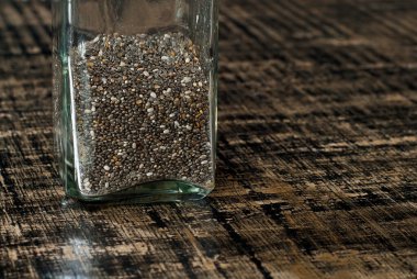 Cam bir kavanozdaki fasulye çekirdeğini yakından çek. Siyah, eski püskü bir tahtada baharatlar. Baharatların yakınındaki metin için boş alan ve kopyalama alanı. Sanatsal bir efekt olarak dramatik ışık karşıtlığı.