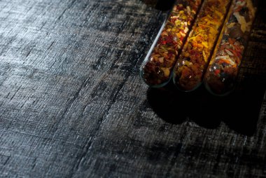 Cam kavanozdaki çeşitli baharatların karışımı. Siyah, eski püskü bir tahtada baharatlar. Baharatların yakınındaki metin için boş alan ve kopyalama alanı. Sanatsal bir efekt olarak dramatik ışık karşıtlığı.